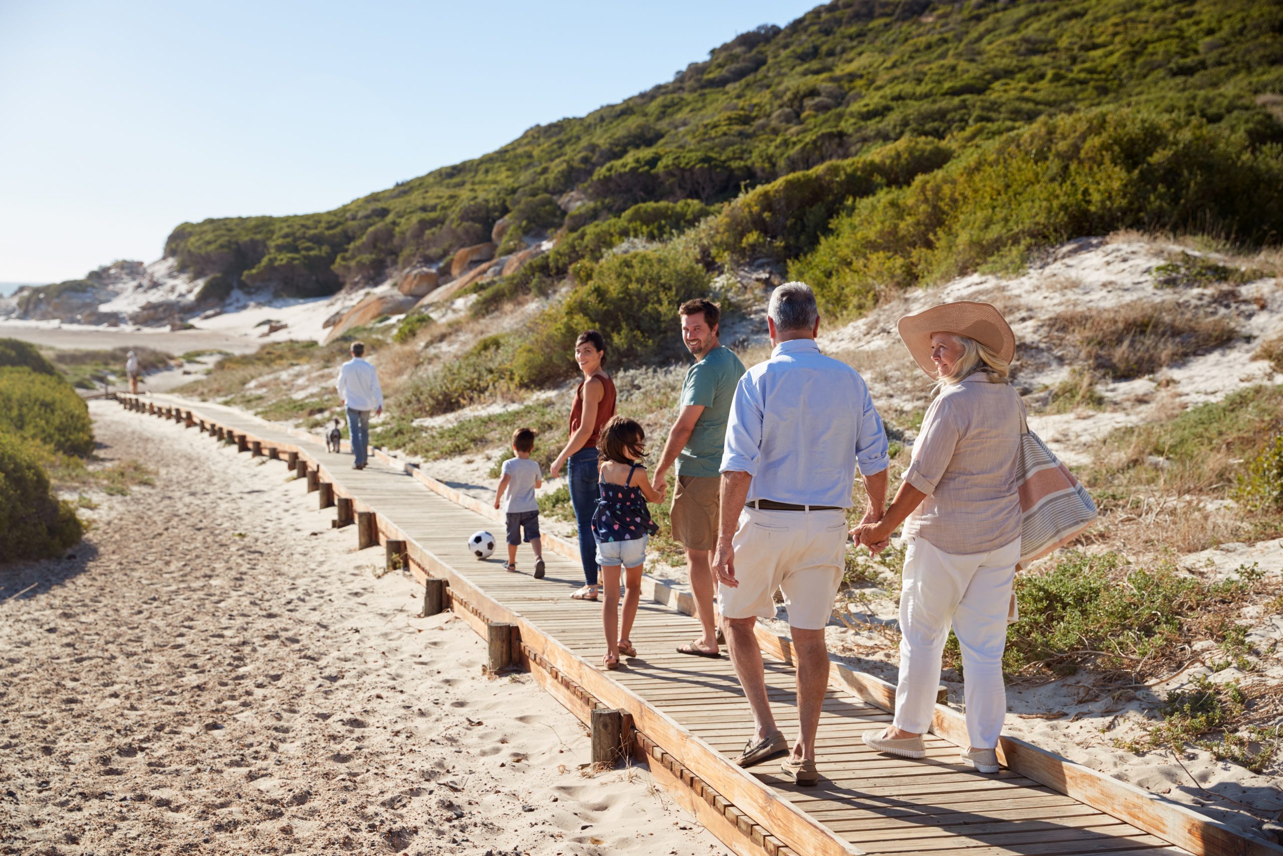 Three generation white family walking together along a wooden promenade on a beach, full length